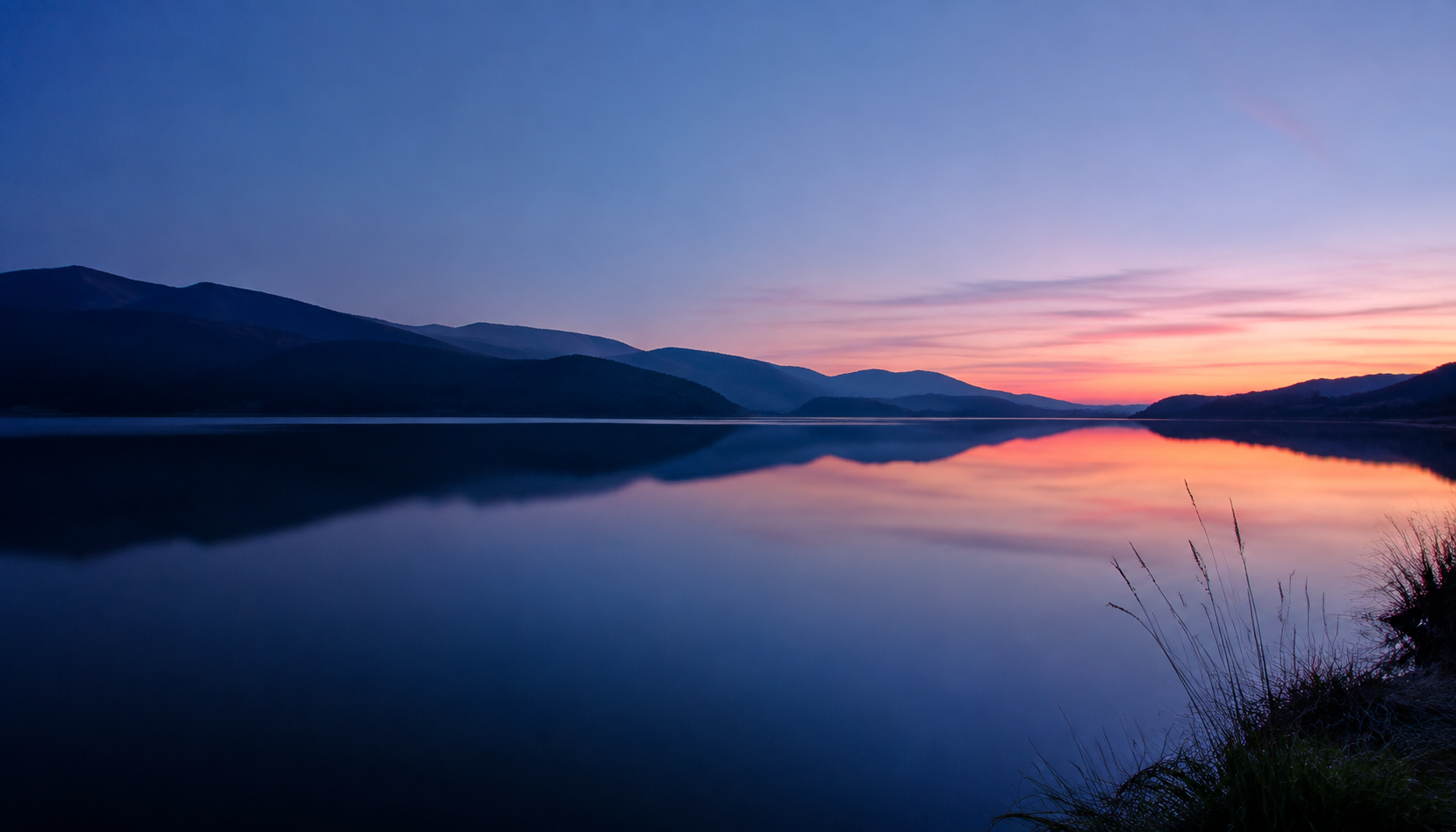 Águas tranquilas de um lago entre montanhas ao pôr do sol